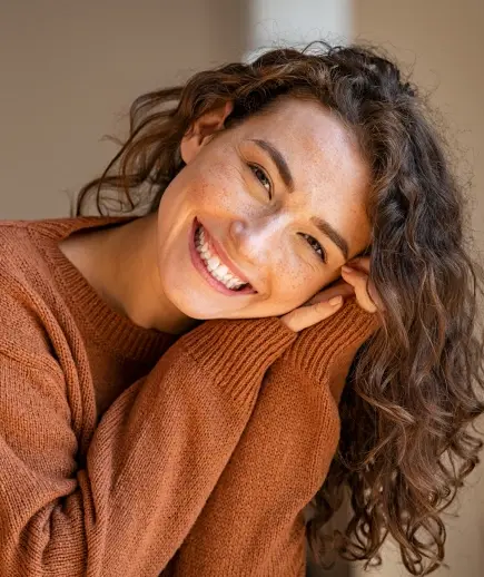 Woman in rust-colored sweater smiling warmly at camera, representing dental patient satisfaction.