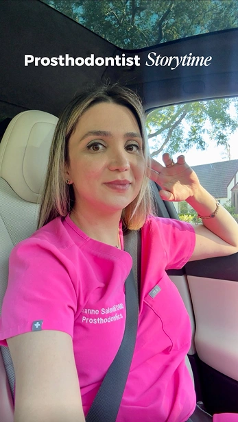 Portrait of a prosthodontist sitting in the dental chair wearing a pink uniform, smiling at the camera.